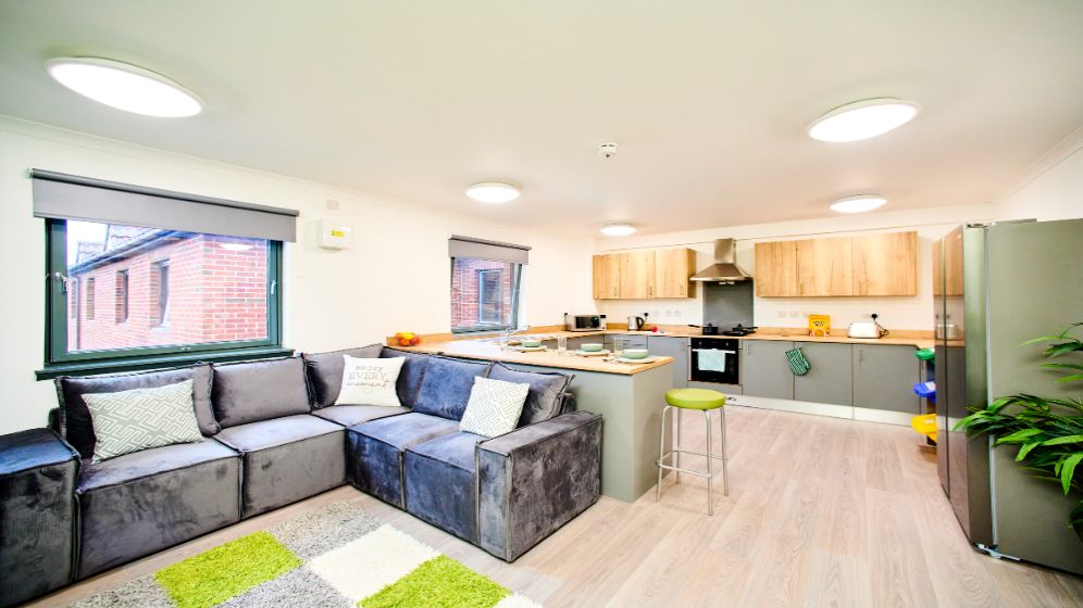 A modern open plan kitchen, with a breakfast bar. There is a large American style fridge and a corner sofa.